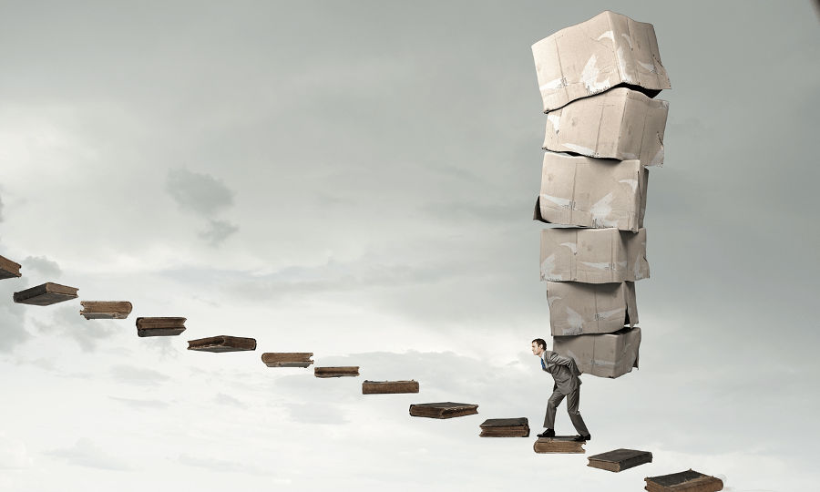 An image of a masc person in a suit, carrying boxes on their back, climbing a floating staircase with grey sky in the background.